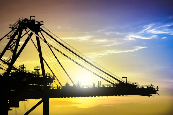 Silhouette of harbour cranes working at sunset in sea port. Cranes and shipyard at port. Silhouettes of shipyard cranes against the background of the sunset sky.