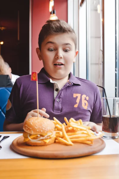 Funny little boy eating a hamburger at a cafe, food concept