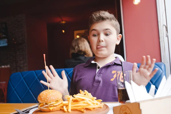 Funny little boy eating a hamburger at a cafe, food concept