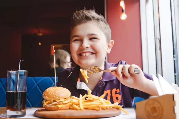 Funny little boy eating a hamburger at a cafe, food concept