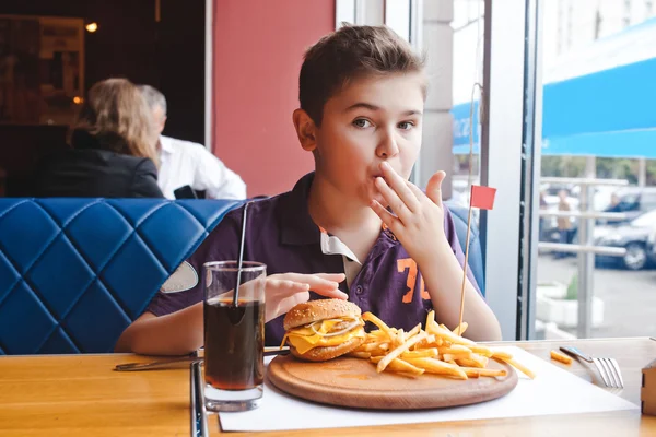 Funny little boy eating a hamburger at a cafe, food concept