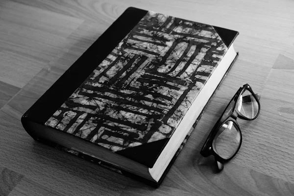 Black book with glasses on table.