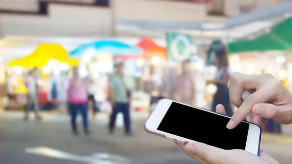 Woman using touch screen mobile phone with blur night Market