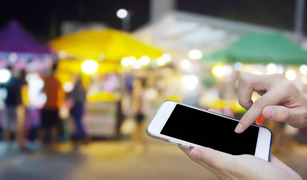 Woman using touch screen mobile phone with blur night Market