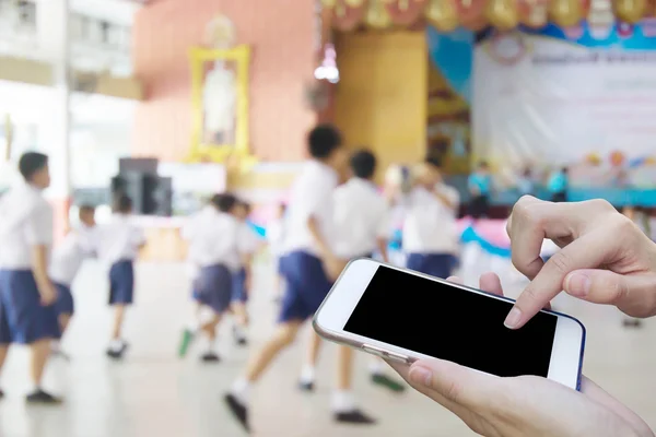 Woman using touch screen mobile phone with blur of student playi