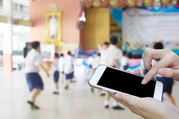 Woman using touch screen mobile phone with blur of student playi