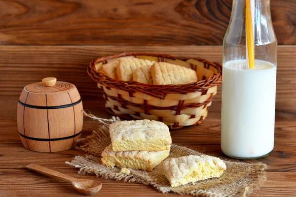 Crispy sweet baked cookies on a wooden table and a wicker basket. Fresh milk in a jar with a straw. Small wooden sugar bowl and spoon. Family breakfast idea