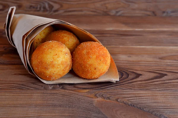 Arancini balls. Fried rice balls in paper on brown wooden background. Snack, sicilian street food