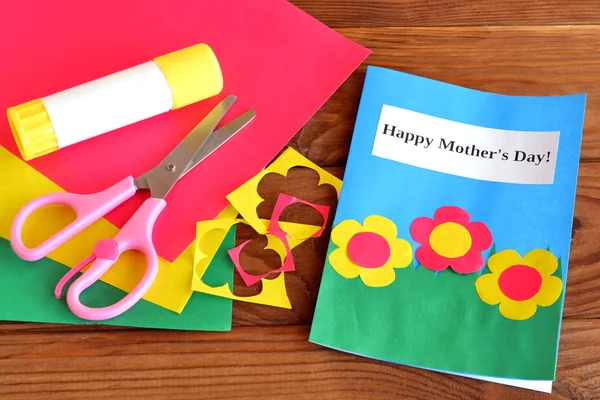 Greeting card Happy mother\'s day - children crafts. Scissors, glue, paper scraps, paper sheets on brown wooden background
