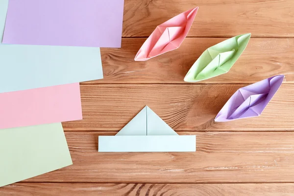 Set of origami boats and square sheets of colored paper on a wooden table. How to make a simple origami ship