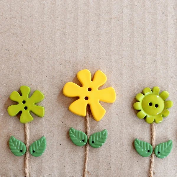 Cardboard background with green and yellow plastic buttons flowers and leaves. Summer fun background with empty copy space for text
