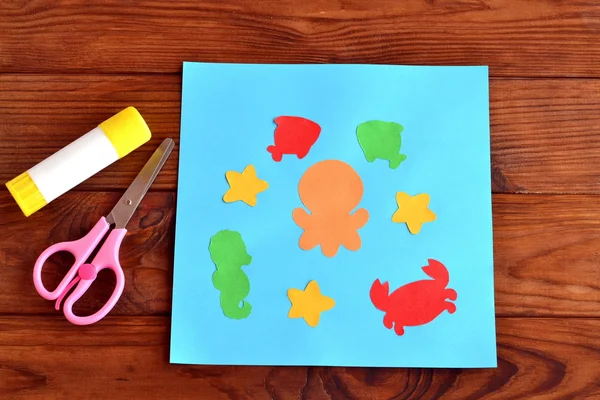 Paper card with sea animals and fishes. Creative ocean creatures crafts for kids. Paper octopus, fish, starfish, seahorse, crab project for children. Scissors, glue on a wooden table