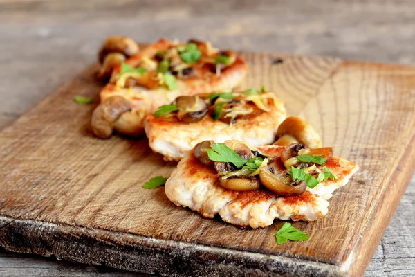 Roasted sliced Turkey breast with cheese, mushrooms and parsley on a cutting Board and an old wooden table. Delicious cooked Turkey meat. Lunch, dinner, picnic recipe. Closeup