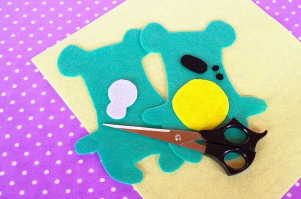 Homemade felt green animal kit, scissors on violet background with polka dots. Sewing project for children. Teddy bear patterns cut from felt. How to make a soft toy at home. Step-by-step