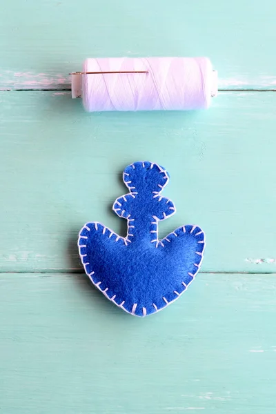 Blue felt anchor ornament and white thread on wooden background. Blanket stitches are used to connect the fabric edges of the toy in a beautiful way. Embroidery crafts for kid. Step. Closeup. Top view