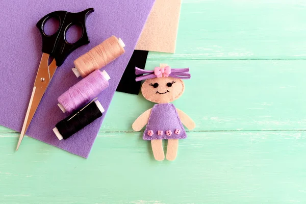 Home made felt doll, scissors, thread, needle, flat pieces of felt on a light wooden background with empty place for text. Sewing craft project. Kids workplace background