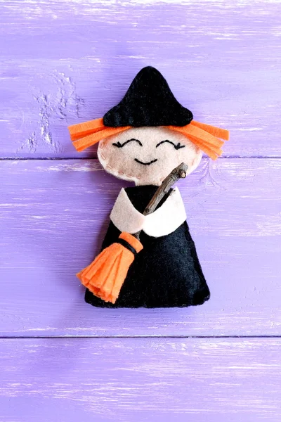 Funny felt witch toy isolated on purple wooden background. Halloween crafts idea for kids. Sewing Halloween doll
