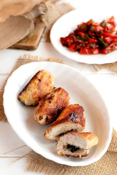 Delicious small meat rolls with mushrooms and cheese. Fried turkey breast rolls with mushrooms and cheese on a plate and on a burlap, cutting board, wooden spoon, vegetable salad. Turkey dinner recipe