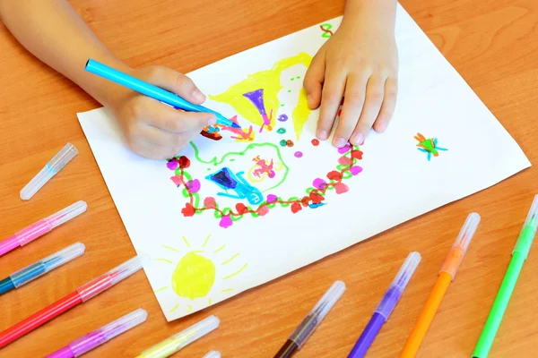 Child draws felt-tip pens. Small child holds a blue felt-tip pen in hand and draws abstract princesses castle. A kids drawing, a set of colored felt pens on a wooden table. Kindergarten art background