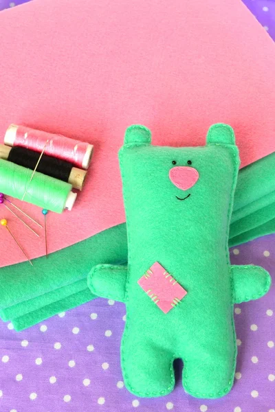 Funny felt bear, thread, needle, pins on fabric background. Home made felt bear. Fun crafts for kids