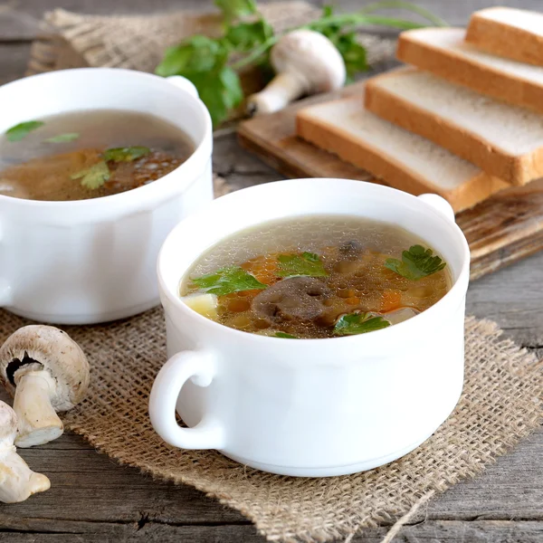 Homemade mushroom soup in a bowl, wheat bread slices on a chopping board, fresh raw mushrooms and green parsley on a wooden table. Diet soup with champignons recipe. Closeup