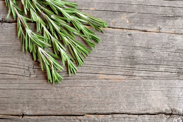 Fresh green rosemary sprigs on a kitchen board and an old wooden background with empty copy space for text. Fragrant herb used in cooking, medicine, cosmetics. Closeup