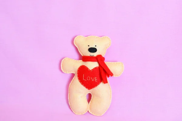 Cute beige Teddy bear on a pink background. Felt beige bear with a red scarf and heart with word Love. Valentine\'s day crafts