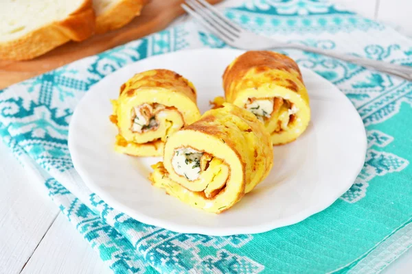 Tasty omelette stuffed with cheese and dill on a plate and a napkin. Sliced bread on a wooden board, fork. Breakfast fried egg rolls recipe