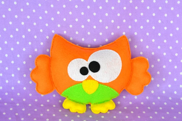 Funny felt owl toy isolated on purple fabric, handmade children crafts