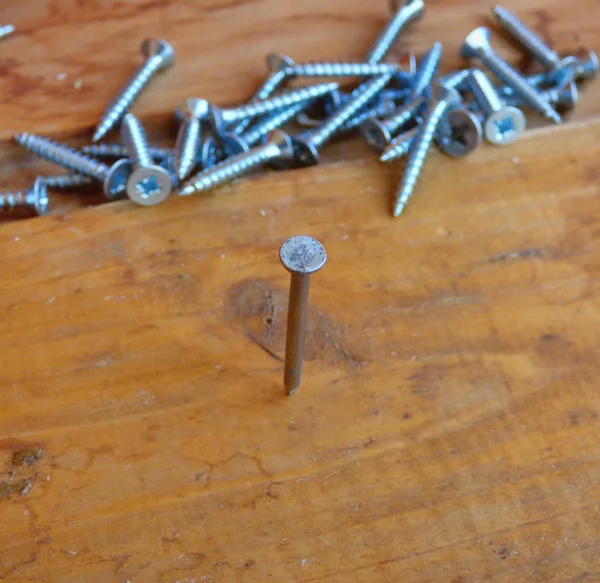Nail hammered in board with fallen screws behind. Soft focus.