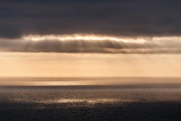 The suns rays pierce the clouds and fall to the Atlantic Ocean, stretching to the horizon