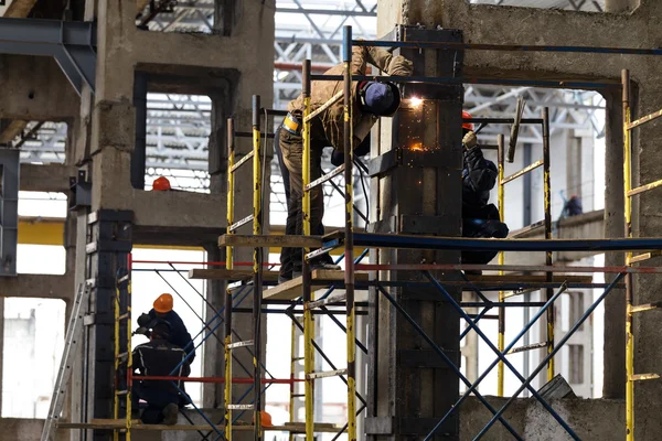 Several workers and welders reinforcing pillars production hall