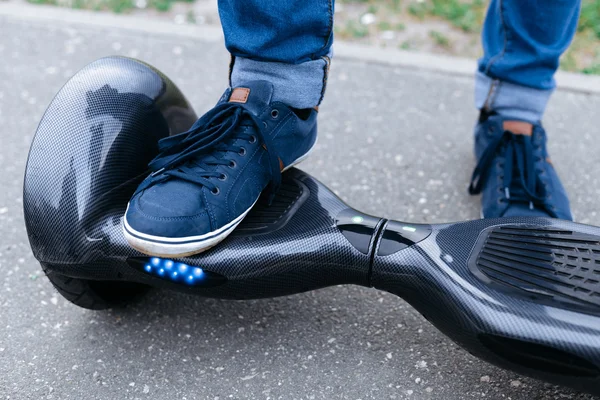 Leg men in blue sneakers and jeans standing on the blue gyroscooter platform, which is on the street. Start to using the electrical scooter, hoverboard, gyroboard or gyroscooter.