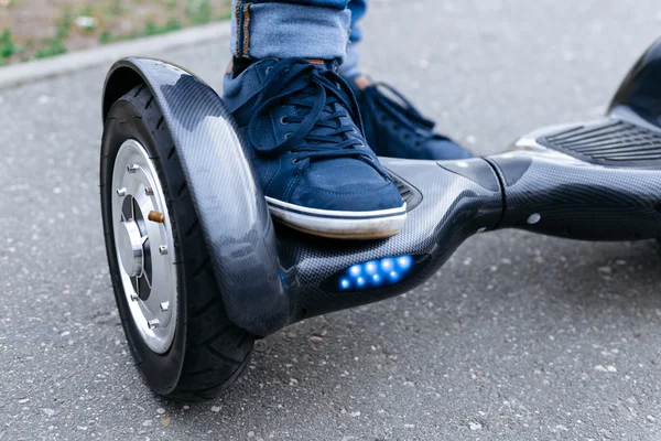 Leg men in blue sneakers and jeans standing on the blue gyroscooter platform, which is on the street. Start to using the electrical scooter, hoverboard, gyroboard or gyroscooter.