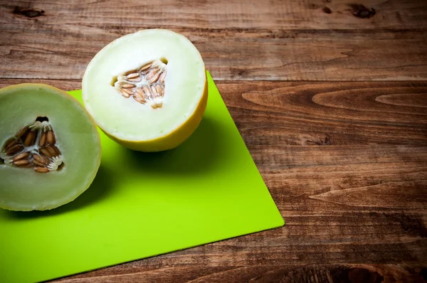 Melon halveson green cutting board, wooden background