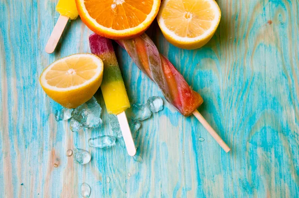 Colorful ice lolly and friuts on blue wooden background