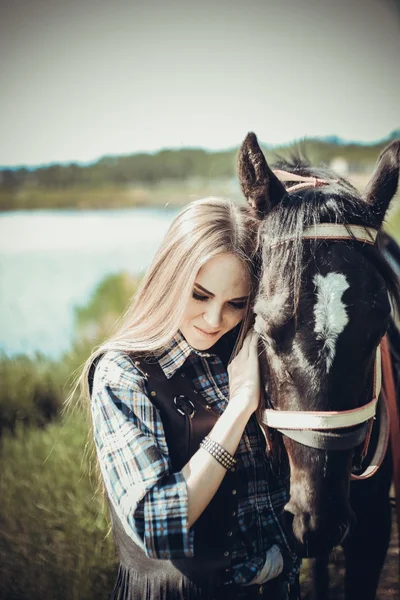 Girl with long hair with a smile leaned the head of standing horse with love