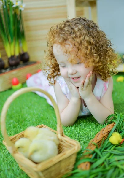 Red-haired blue-eyed girl is happy and smiling to two little chicks in a basket