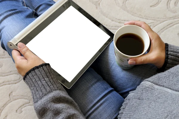 Young woman holding a tablet and a Cup of coffee sitting on the carpet and lying next to a Notepad.The concept of online shop