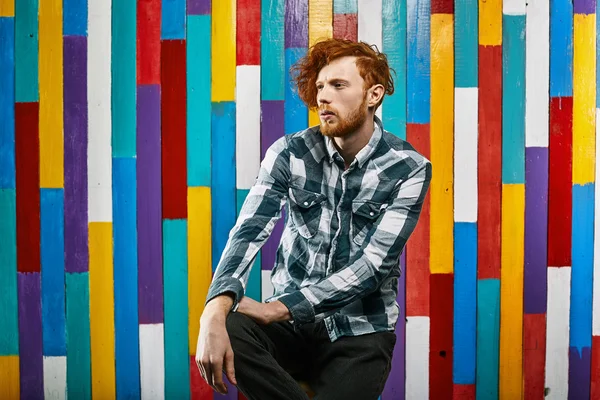 Young thoughtful redhead bearded man in plaid shirt on colourful
