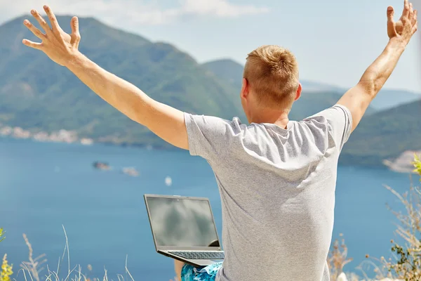 Young freelancer using laptop sitting near the sea.Happy smiling man working online.Studying and learning using notebook computer.Freelance work,business people concept.