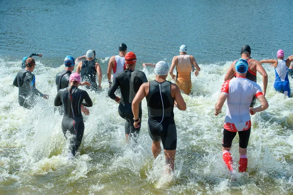 Group triathlon participants running into the water for swim por