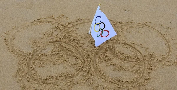 Olympic rings drawn in the sand and olympic flag in the centre