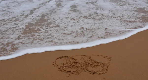 Wave approaches olympic rings drawn in the sand