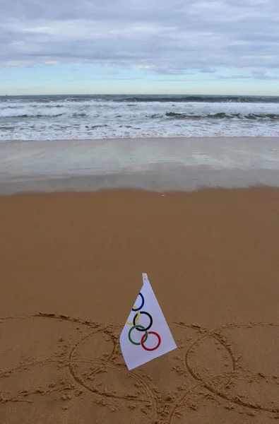 Olympic rings drawn in the sand with an olympic flag.