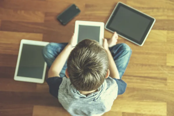 Little boy using tablet sitting on wooden floor. Digital tablets, mobile phones all around. Selective focus. Toned image. Top view. Education, learning, technology concept