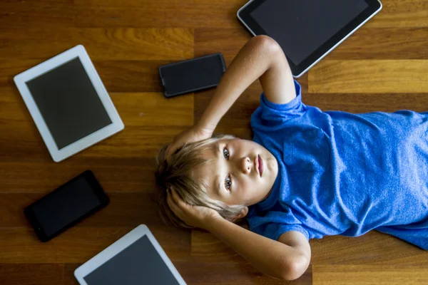 Little boy sad, tired and stressed with tablet computer PC. Kid holding his head. Tablets, mobile phones, laptop all around. Top view. Education, learning, technology, addiction concept. Toned image