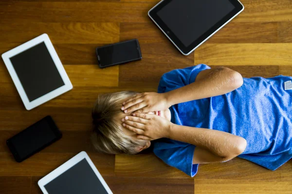 Little boy sad, tired and stressed with tablet computer PC. Kid holding his head, close eyes. Tablets, mobile phones around. Top view. Education, learning, technology, addiction concept