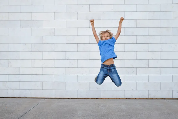 Happy little boy jumping. Urban gray background. People, childhood, happiness, freedom, movement concept