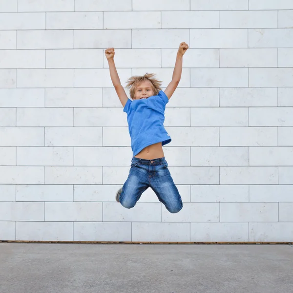 Happy little boy jumping over gray urban background. People, childhood, happiness, freedom, movement concept